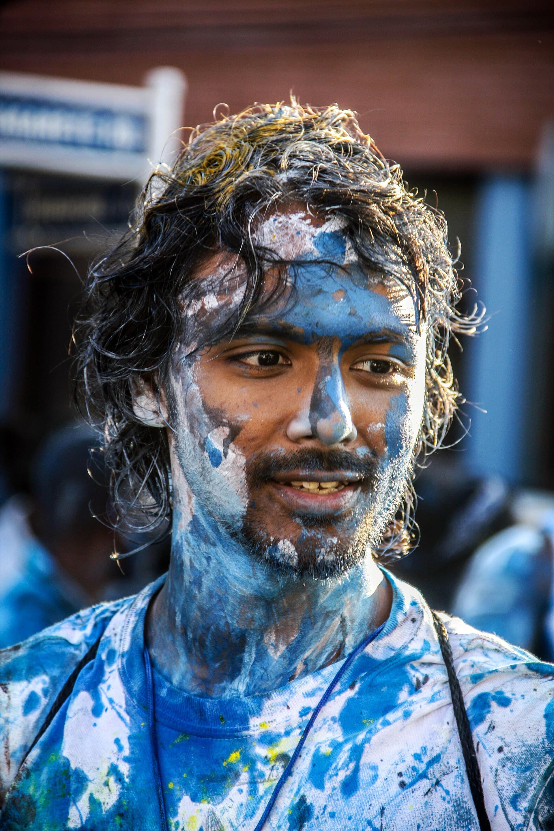 Close-up of a smiling J'ouvert reveller in Trinidad on J'ouvert morning 2015, his face, beard and hair splattered with blue and white paint, wearing a paint-covered T-shirt